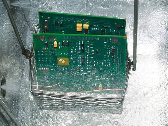 A basket of PCBs being raised out of the solvent in the rinse sump on a vapor degreaser